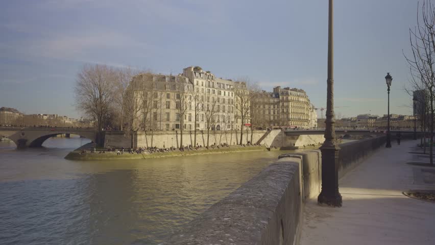 Seine River in Paris, historic stone bridge, people enjoying sunny winter day long shore. Panning