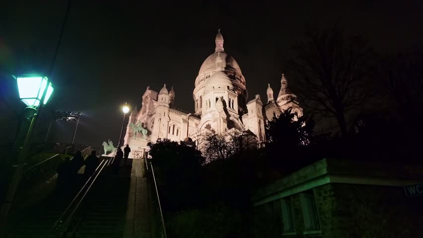 Stunning low-angle view of Sacré-Cœur Basilica at night, silhouette of figures climbing Montmartre stairs, mystical and cinematic atmosphere, Paris, France. Slow-motion