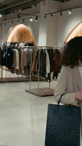 Vertical view of two multi-ethnic young girl friends holding bags with clothing items walking around womens store in shopping centre