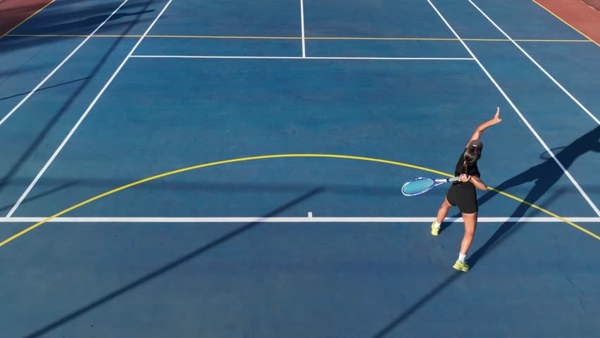 Brunette woman smashes ace tennis serve on blue clay tennis court