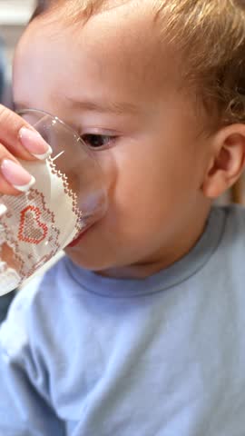 Toddler learning independent drinking, showing various expressions while mastering water glass in kitchen, demonstrating childhood developmental milestone with joyful gestures
