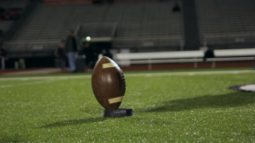 Football player practicing kicking off, on a turf field at night.