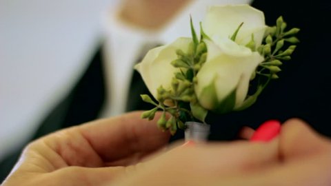 Close up of a woman pinning a corsage on a man in a black suit
