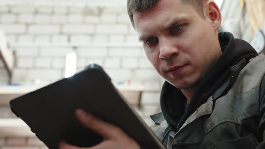 Professional car engineer carefully reading digital instructions on tablet, preparing for precise wheel change within modern auto repair shop workspace
