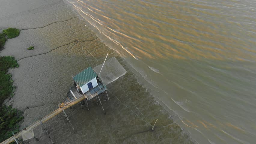 Carrelet fishing hut with fishing net over peaceful estuary, Garonne in France. Aerial top-down view