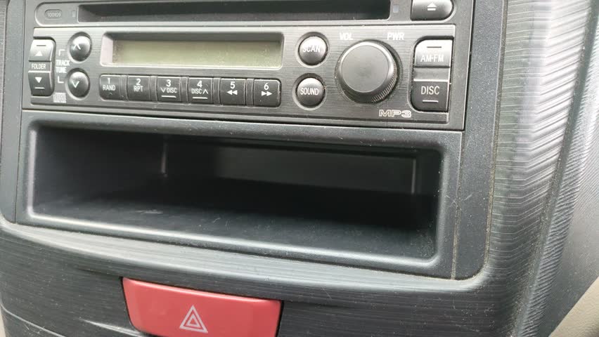 A close-up of a hand pressing a button on a car radio. The dashboard features an old-school audio system with buttons and a digital display. Ideal for themes of transportation, technology
