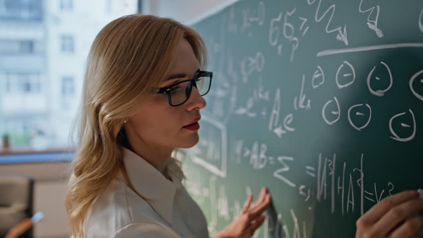 Algebra educator writing on chalkboard explaining mathematical formulas in school class closeup. Serious woman teacher in glasses teaching math in college classroom. Female university professor work. - Powered by Shutterstock - Get 15% off with code: PIKWIZARD15