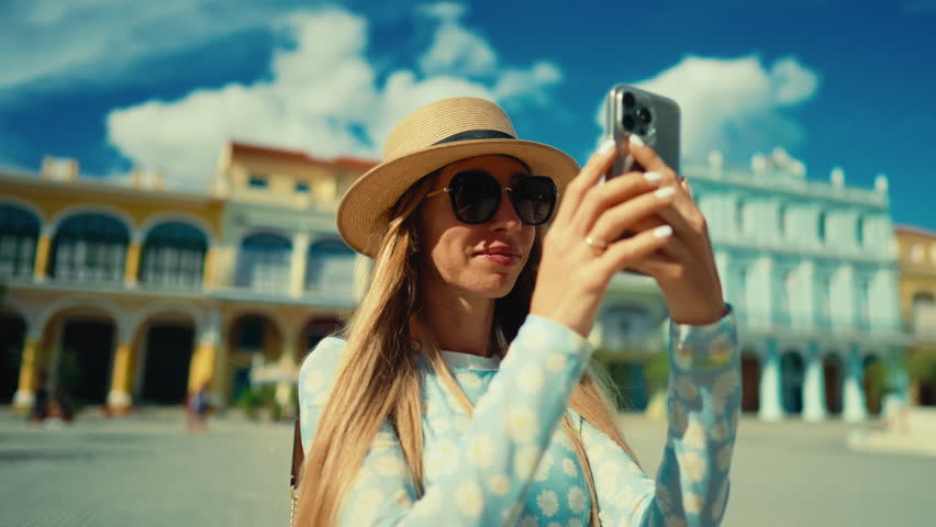 Blonde woman tourist taking picture by smartphone of old landmark in downtown. Portrait of happy female traveler with mobile phone, photographing and sightseeing in main square of old european town