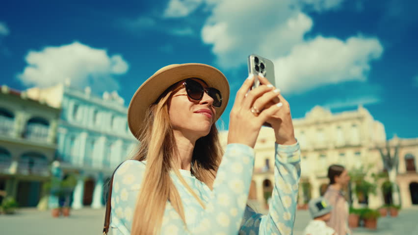 Blonde woman tourist taking picture by smartphone of old landmark in downtown. Portrait of happy female traveler with mobile phone, photographing and sightseeing in main square of old european town