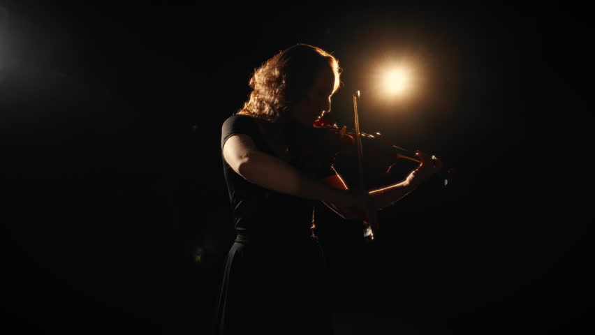 Fascinating classical music concert in darkness, beautiful woman playing violin. Solo of female violin player on stage of theatre, romantic music and melody, inspiration by sounds, silhouette of lady