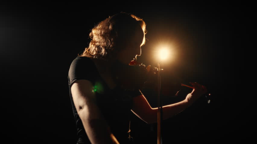 Talented woman performing beautiful classic melody by violin, silhouette in dark . Concert in music-hall, solo performance of inspired female musician, romantic love song, contemporary performance
