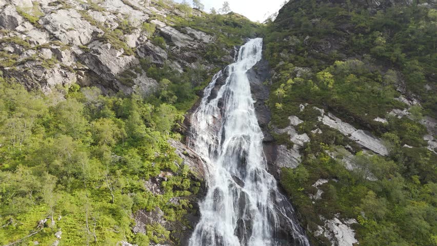 Aerial drone views capture Steall Falls plunging from rugged Highland cliffs into the valley below. A breathtaking sight of raw nature, surrounded by lush greenery and dramatic mountain landscapes