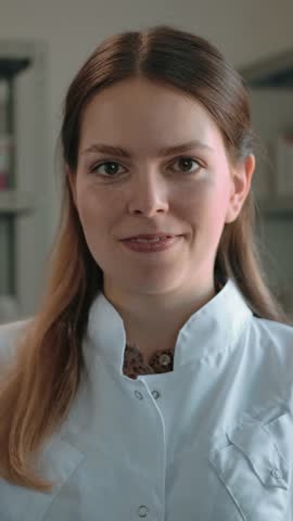 Woman pharmacist shows to the camera the COVID-19 coronavirus vaccine. Portrait of a cute woman in a white coat in a pharmacy interior smiling with a medicine ampoule in her hand. Slow motion
