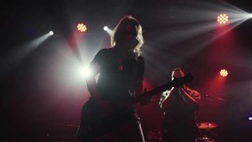 Female guitarist playing electric guitar on stage with a singer in the background, illuminated by stage lights in slow motion - Powered by Shutterstock - Get 15% off with code: PIKWIZARD15