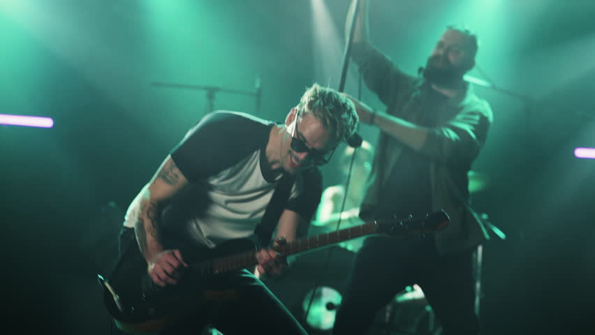 Skilled guitarist performing dynamic electric guitar solo on concert stage, bathed in vivid green lighting while delivering passionate rock performance in dramatic slow motion