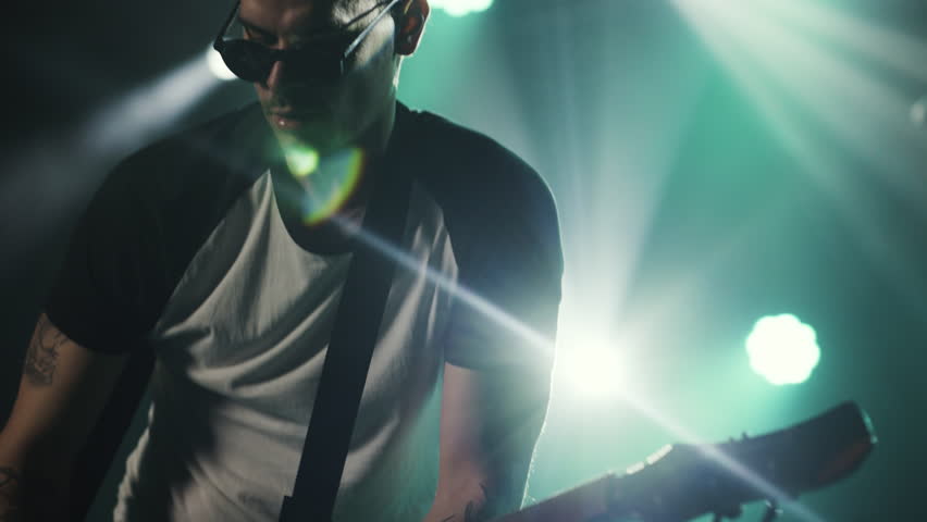 Skilled guitarist performing dynamic electric guitar solo on concert stage, bathed in vivid green lighting while delivering passionate rock performance in dramatic slow motion