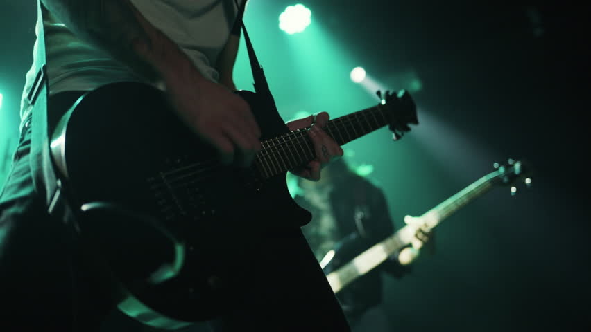 Close up slow motion of a guitarist playing electric guitar during a live concert under green stage lights