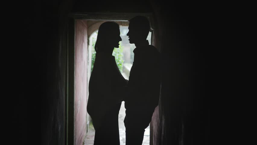 Silhouette of romantic couple kissing in dark alleyway