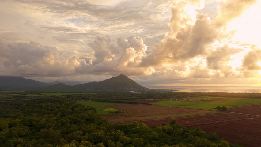Dramatic sunset over tropical mountains and fields in Mauritius.Golden sunlight illuminating island landscape and coastline.
