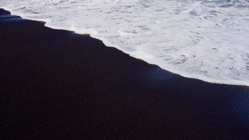 Serene Waves Gently Lapping on a Picturesque Black Sand Beach during a Tranquil Day