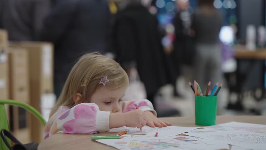 A child is in the Kids Area of ​​the shopping mall while parents are busy shopping. Childcare service. Little girl draws alone.