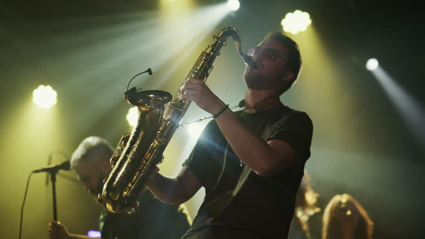 Slow motion footage of a saxophonist playing with energy during a live concert, illuminated by stage lights