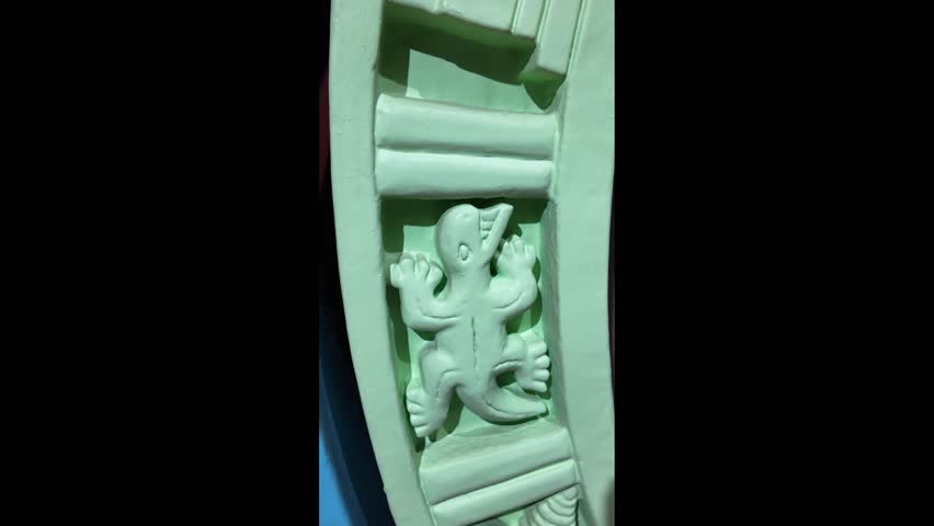 A green lizard is sitting on a white background. The lizard is small and has a long tail. It is positioned in the center of the image, with its head slightly tilted to the left