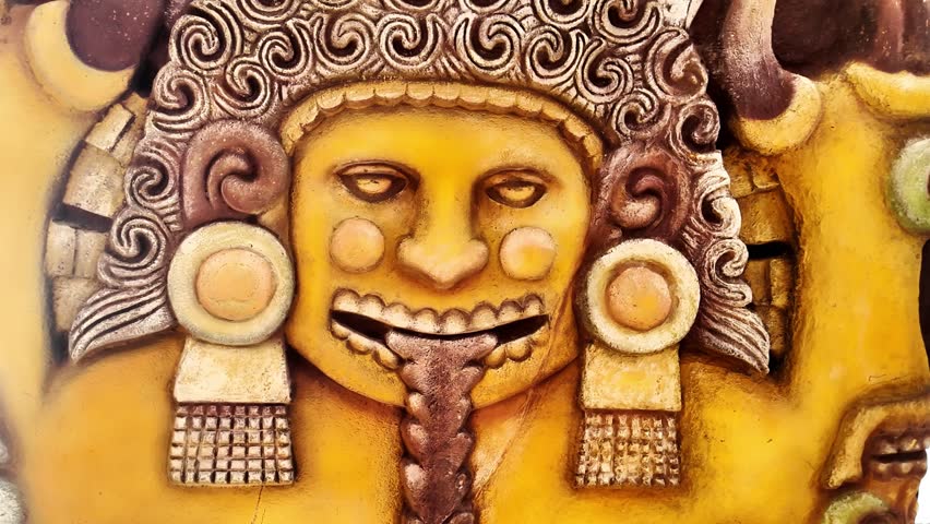 A man with a long tongue is shown in a yellow color. He is wearing a gold colored headdress