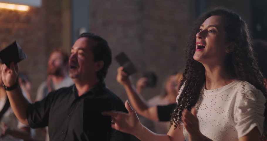 Man of Hispanic descent raising offering envelope in church worship, smiling with joy, illuminated cross in background, diverse congregation in spiritual celebration and unity