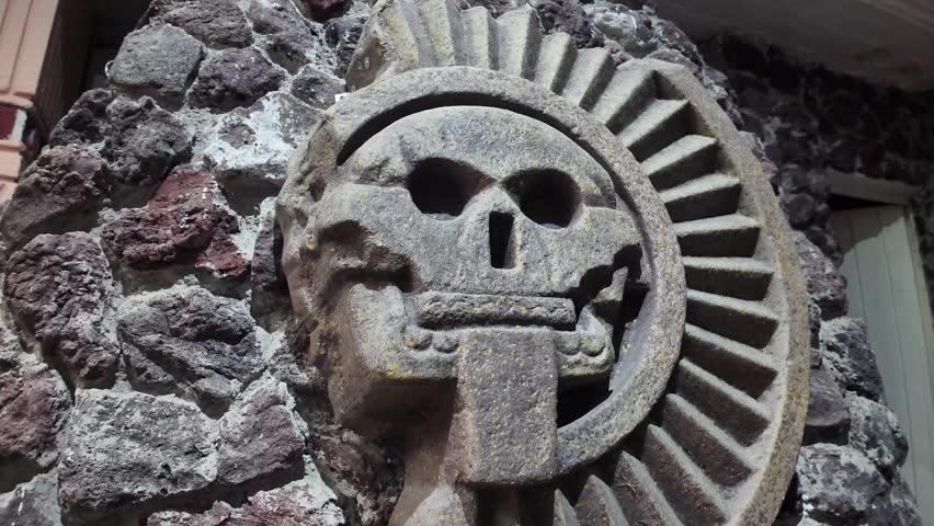 MexicoCity, Mexico 03172025  A skull is carved into a stone. The skull is surrounded by a circle of stone. The circle is carved with a spiral design