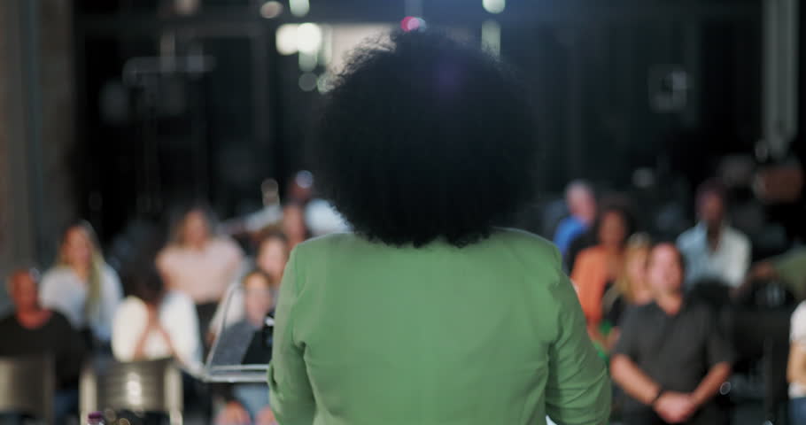 Back view of a woman delivering a speech to an engaged audience, inspiring spiritual gathering, diverse crowd listening attentively to community leader