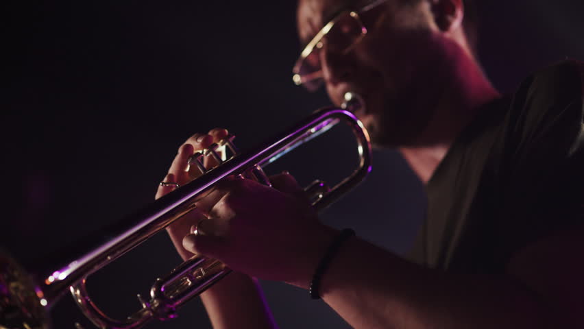 Dark stage bathed in purple light revealing skilled trumpet player performing intense musical moment with dramatic closeup slow motion capturing passionate artistic expression
