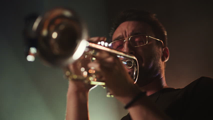 Trumpet player performing soulful solo in warm backlighting, revealing passionate musical expression during dark stage performance