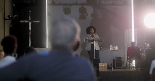 Woman speaking at a church event, with a cross in the background and attendees listening attentively, focus on her as she engages the crowd in a religious setting - Powered by Shutterstock - Get 15% off with code: PIKWIZARD15