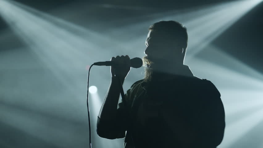 Silhouette of a male singer holding a microphone and performing on stage under spotlights, slow motion