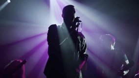 Male singer performing passionately with band under vibrant purple stage lights, capturing electrifying live music moment in slow motion - Powered by Shutterstock - Get 15% off with code: PIKWIZARD15