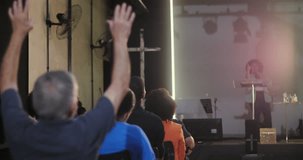 Man in the audience sitting with his back to the speaker, paying attention to a woman giving a sermon or speech at a church event, cross in the background - Powered by Shutterstock - Get 15% off with code: PIKWIZARD15