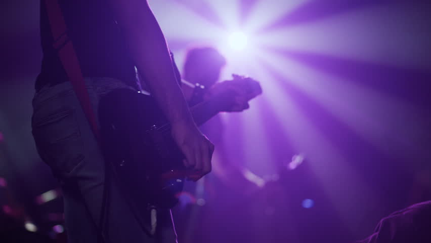 Passionate guitarist performing electric guitar riff under vibrant purple lights, embodying raw musical energy during intense stage performance
