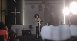 Woman passionately speaking at a church event, addressing the audience with a microphone, cross in the background, and people listening attentively - Powered by Shutterstock - Get 15% off with code: PIKWIZARD15