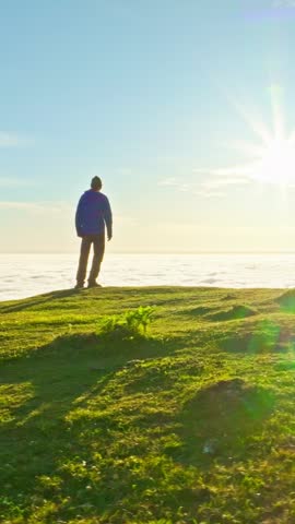 Aerial drone shot of man silhouette standing on hill enjoying looking at sunrise in mountains hill above clouds. Clouds Inversion. Madeira, Portugal. Orbiting orbit shot