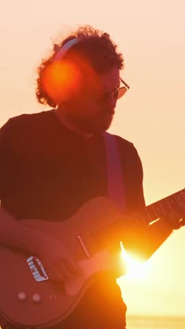 Hipster street musician in black playing electric guitar in street outdoors on sunset silhouette with lens flare and light leak