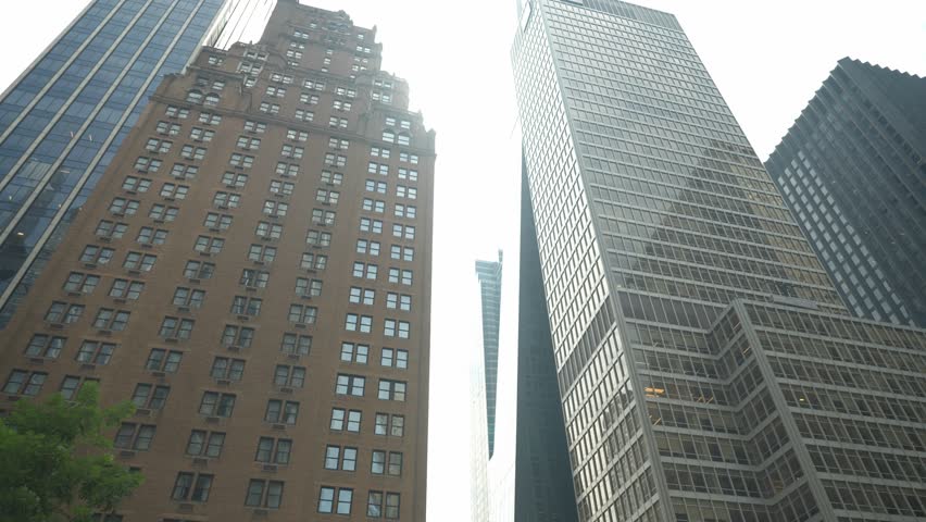 Tall buildings reflect sunlight while people walk below in a busy city. The mix of architecture showcases modern design against historical structures. Life thrives in this urban landscape.