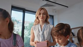 Woman teacher guiding art lesson in primary school. Young lady helping pupils in creative work bringing materials for drawing in classroom. Enthusiastic children focused on crafts creating in class. - Powered by Shutterstock - Get 15% off with code: PIKWIZARD15