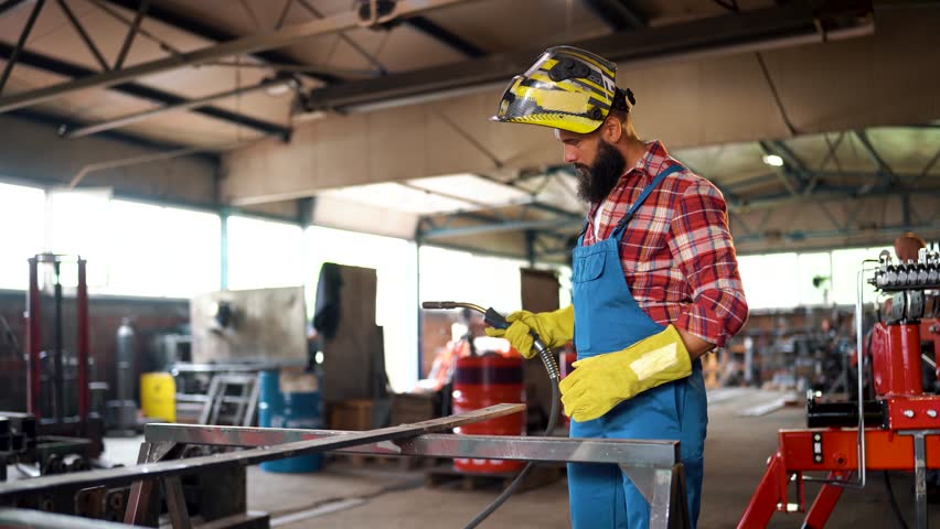 Professional metalworker donning protective gear, wearing safety helmet and gloves while preparing for welding work inside industrial workshop