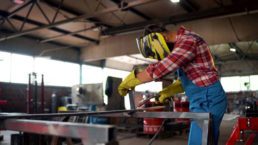Skilled welder wearing protective gear meticulously joins metal parts using specialized equipment in a bustling workshop