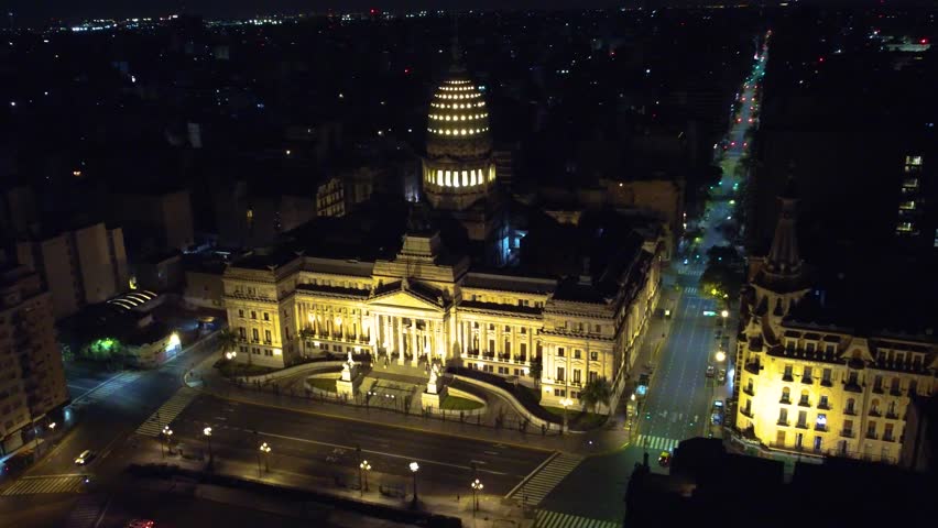 "Drone night view of the National Congress of Argentina in Buenos Aires, showcasing its illuminated neoclassical architecture and urban surroundings. Iconic government building and city landmark
