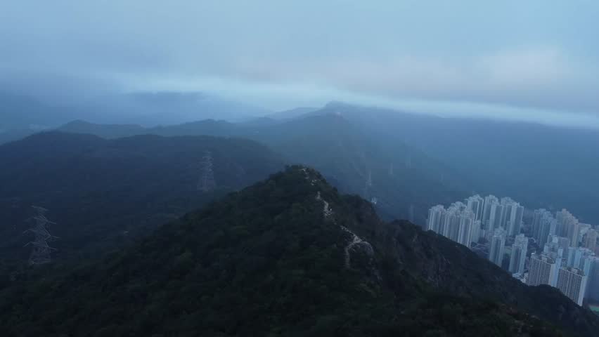 Aerial drone footage gliding over a mountain near Hong Kong Called Lion rock during a cloudy evening day. The area is surrounded by mountains and the air is polluted with smog or it is misty or foggy.