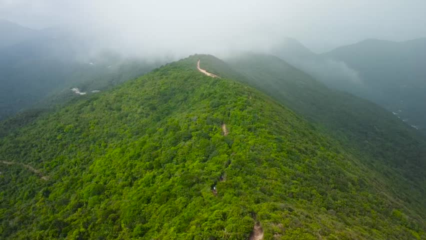 Aerial drone footage rising up over a mountain in China Asia called Unicorn ridge while white fluffy clouds and mist is hovering in between the mountains. A dirt muddy brown road going up the hillside