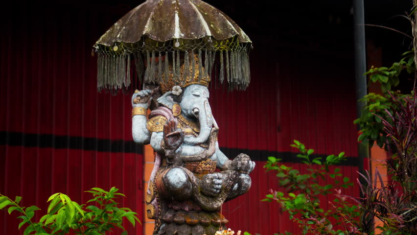 An old hindu stone statue of Ganesha covered with moss, standing on the street on the Bali island in indonesia