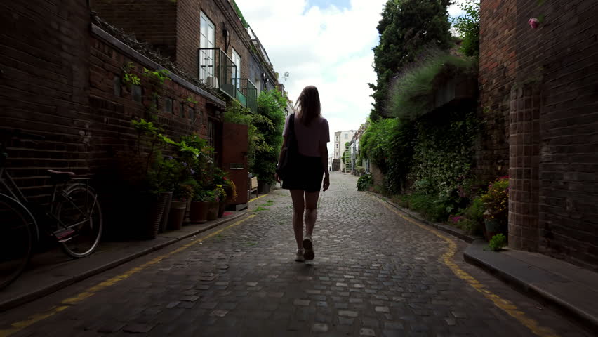 Follow footage rear view of silhouette of unrecognizable young woman in shorts walking forward in archway in old part of town. tourist traveling in city.